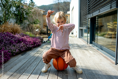 Toddler boy playing with basketball outdoors in backyard near home.