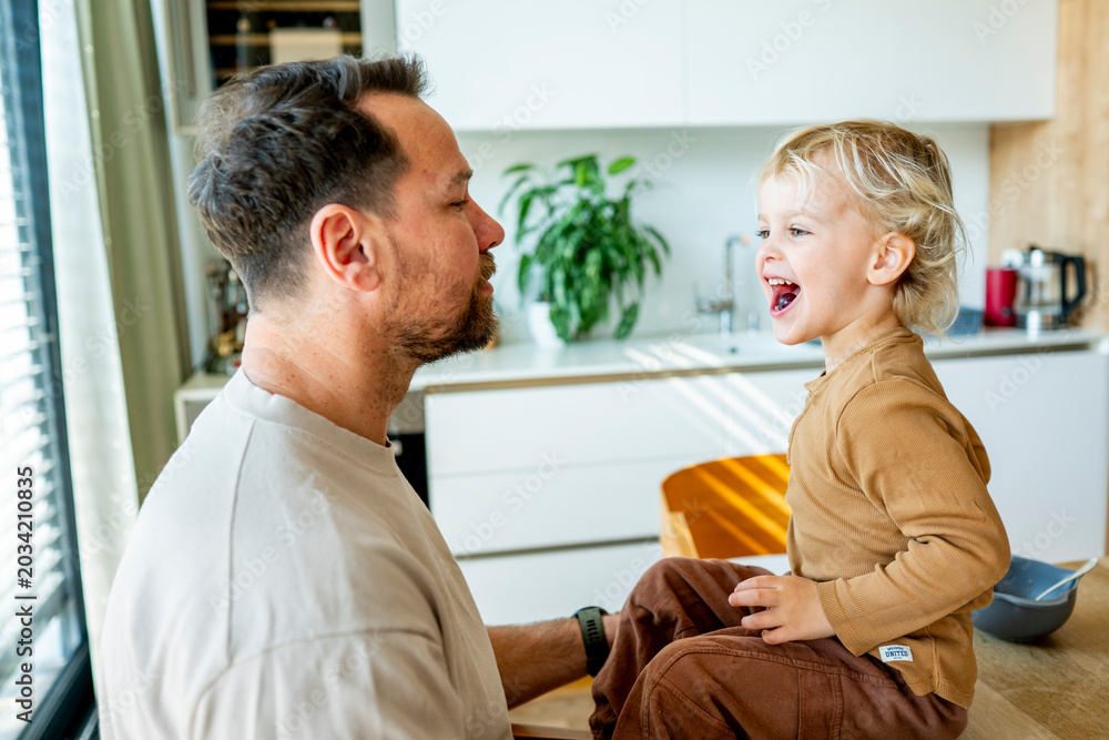 Obraz premium Dad feeding toddler during family mealtime in modern kitchen.
