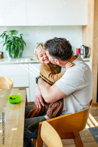 Dad feeding toddler during family mealtime in modern kitchen.