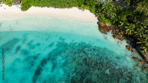 Turquoise lagoon with coral reefs meets a white sand beach surrounded by lush green vegetation. Seychelles, Mahe. Petite Anse.