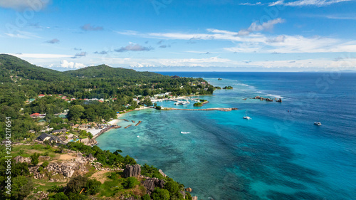 Turquoise water meets lush green coastline with boats anchored near the shore. Seychelles, La Digue.