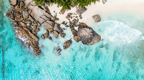 Crystal clear turquoise water with visible rock formations and a sandy beach, surrounded by greenery. Seychelles, La Digue. Anse Patate.