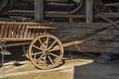 Tableau sur toile Old traditional wooden cart with a wheel in front of a rustic log barn