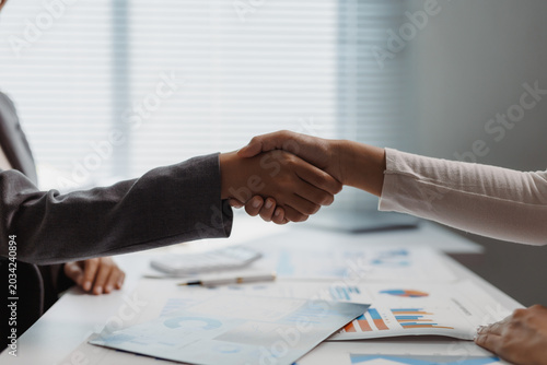 Fotografie Two business colleagues shaking hands over a desk with documents, agreeing on a