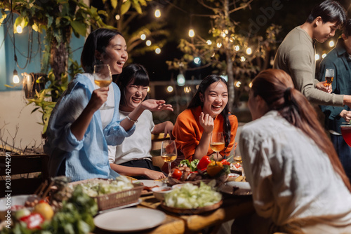 Happy asian friends gathering for an evening outdoor dinner party, sharing food and drinks, laughing and socializing