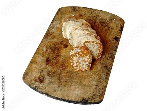 Aged fermented tempeh arranged on a worn wooden chopping board isolated on white background, traditional Indonesian tempe busuk ingredient for authentic local cuisine