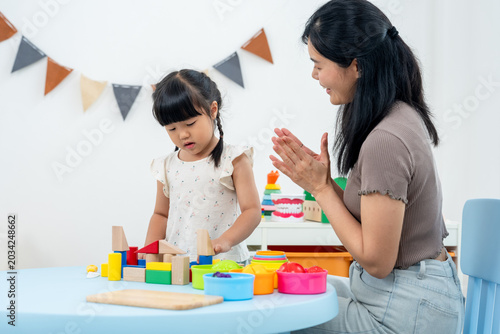 Fotografía Asian mother applauds preschool daughter building wooden blocks at table, encouraging confidence, concentration, constructive play, warm bonding, early development activity during home learning