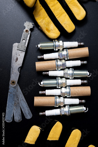 Eight sparkplugs on a table with feeler gage and gloves