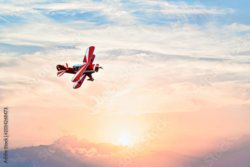 A red aerobatic biplane performing air shows against an orange sunset sky. Classic airplanes