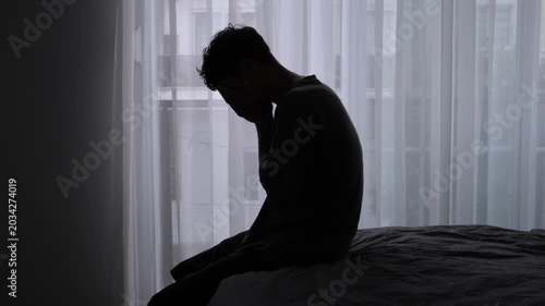 Burnout and emotional exhaustion silhouette of lonely young man sitting on bed near window feeling depressed disconnected and mentally overwhelmed at home