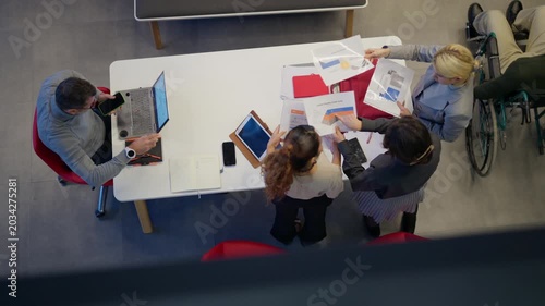 A diverse team collaborates around a white table, reviewing documents and using digital devices. Business professionals engage in a productive meeting, discussing plans and sharing ideas.