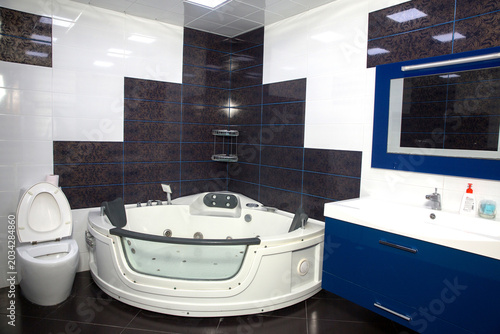 stylish dark patterned wall tiles, creating a luxury spa-like atmosphere for home relaxation . Modern bathroom interior featuring a large white round jacuzzi tub, blue vanity cabinet with sink, and