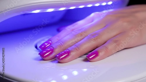 Woman's hand with vibrant purple nail polish being cured by a UV lamp during manicure process