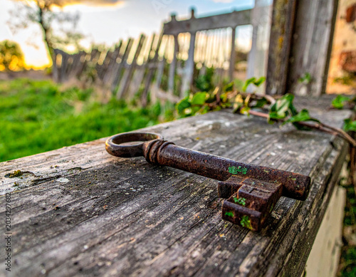 Close-up of an old rusted iron key lying on a weathered wooden window sill outside.