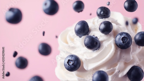 A close-up of whipped cream topped with fresh blueberries against a soft pink background.