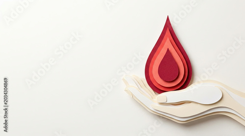 Red blood drop held by a paper cut hand on neutral background for World Blood Donor Day, health campaigns, awareness initiatives, and charity projects