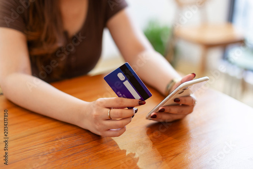 Young woman making mobile payment using smartphone and credit card at table. Modern digital banking and online purchase concept.