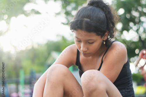Canvas Print Focused Latina preteen girl sitting in park while loosening roller skate straps