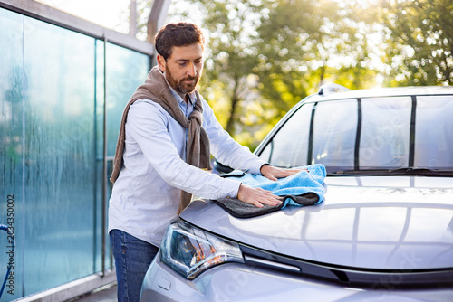 Photos A man with a beard is carefully drying the hood of a car with a blue microfiber