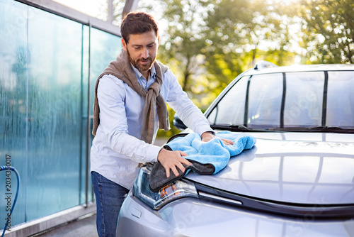 Obraz na płótnie A caucasian man is carefully polishing the hood of his car with a blue microfibe