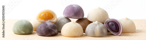 moist colorful mochi desserts varying shapes sizes stacked haphazardly across warm beige surface soft diffused