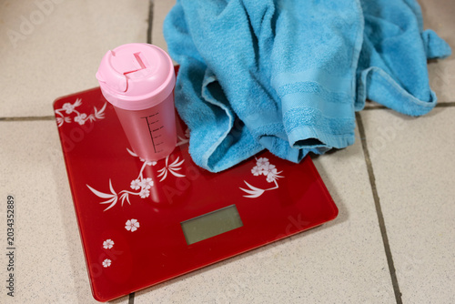 Canvas-taulu Pink shaker bottle and blue towel on a red digital scale in a bathroom