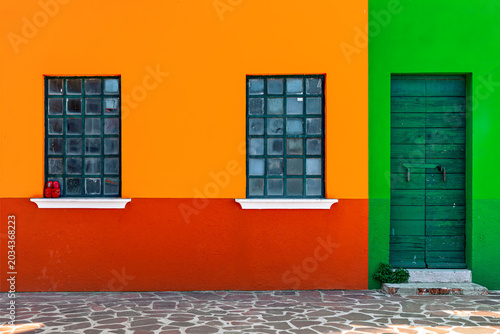 Red, green and orange wall, two square windows and green wooden door on the island of Burano, Italy