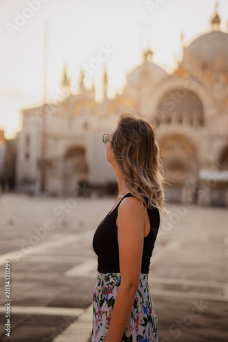 Stylish young woman in profile with windswept hair gazing up at the golden St. Mark's Basilica in Venice, Italy at beautiful warm sunset light