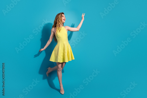 Slika na platnu Pretty young woman in a yellow dress posing against a blue background with a che