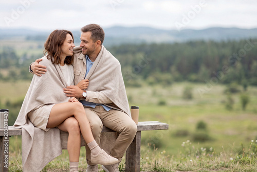 Cozy Couple Wrapped in Blanket with Coffee on Scenic Mountain Viewpoint, Smiling Together
