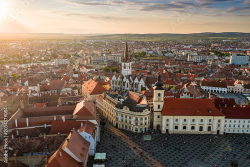 Aerial panorama of the old town of Sibiu featuring historic red roofs and the tall church tower, with the majestic blue Fagaras mountains visible on the horizon. Romania Transylvania, landscape.