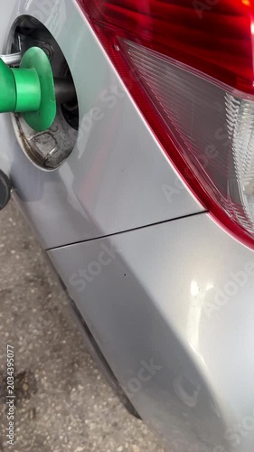 Vertical video. Close up of pump nozzle, filling up car fuel tank with unleaded petrol, gas.