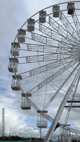 Vertical shot. Static ferris wheel, cabins swinging in the breeze, observation wheel empty with no people in amusement park.
