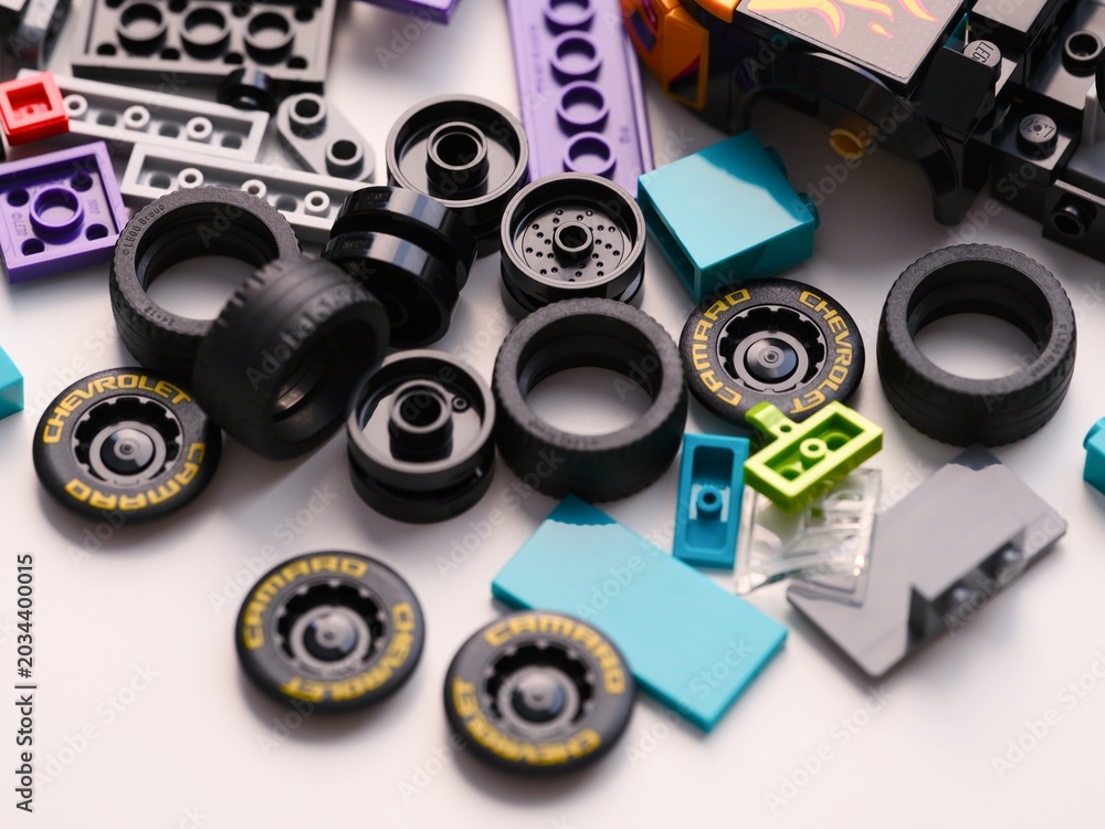 Obraz premium Tambov, Russian Federation - January 01, 2026 A pile of Lego black plastic toy Chevrolet Camaro car wheels, tires, and colorful bricks scattered on a white surface.