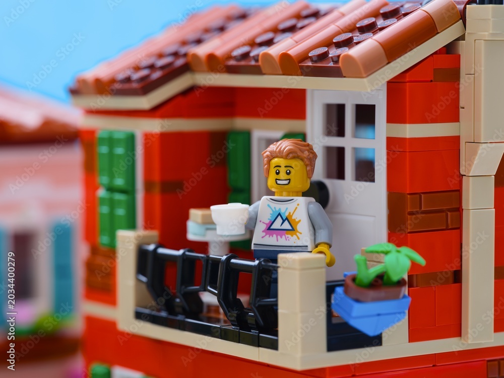 Obraz premium Tambov, Russian Federation - January 04, 2026 Lego man minifigure with a white cup standing on a balcony in a Mediterranean city.