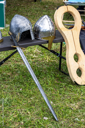 Photography Medieval helmets and a sword displayed on a table with a wooden shield in a gras