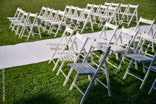 View of white wedding chairs and a white aisle runner on a grassy lawn for a ceremony, Poland, Europe.