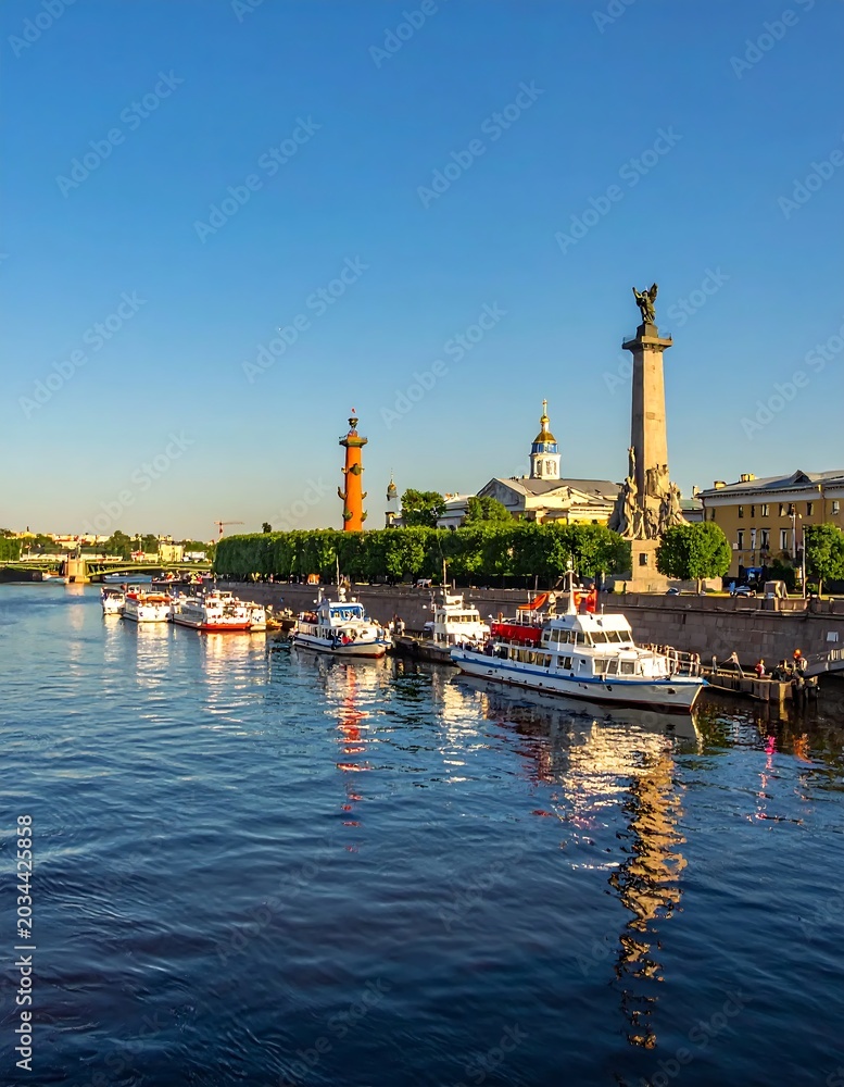 Fototapeta premium Historic Riverside Promenade with Moored Boats and Tall Monument Under Clear Blue Sky