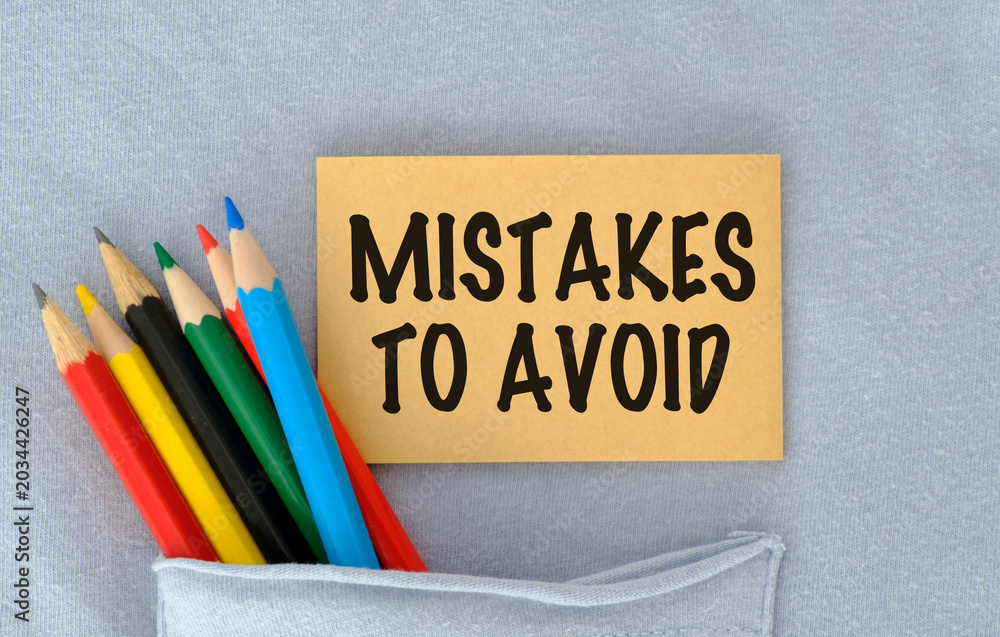 © Pawel - Colorful pencils lean near a sticky note. Note reads MISTAKES TO AVOID in bold black letters. Note rests in a folded fabric pocket.