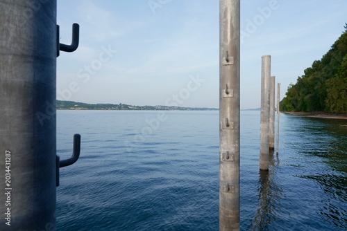 Obraz na płótnie Calm Lake Constance view with metal mooring posts and forested shore