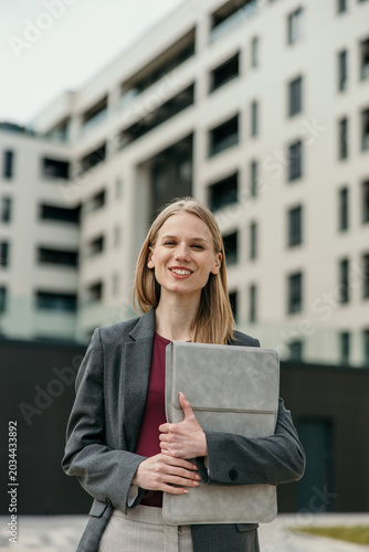 Принти на полотні Elegant business professional woman holding laptop outside modern building