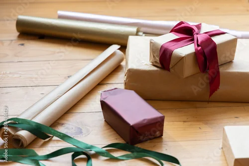 Fototapeta Close-up scene showing stacked kraft-paper wrapped gift boxes with deep-red satin bow on tabletop