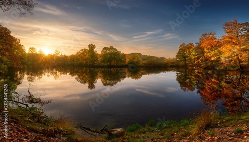 Autumn Sunset Reflects On Calm Water In A Lush Forest Casting A Golden Glow On Trees And Creating A Scenic Peaceful Landscape During Twilight Hours