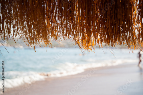 Bild auf Leinwand Straw beach umbrella hangs above sandy shoreline with blurred sea background during sunny summer vacation