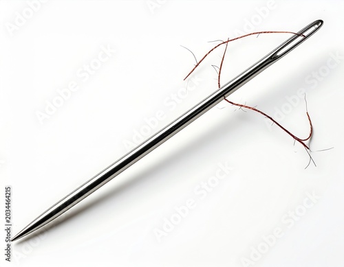 Close-up macro shot of a silver sewing needle with red thread on a white background