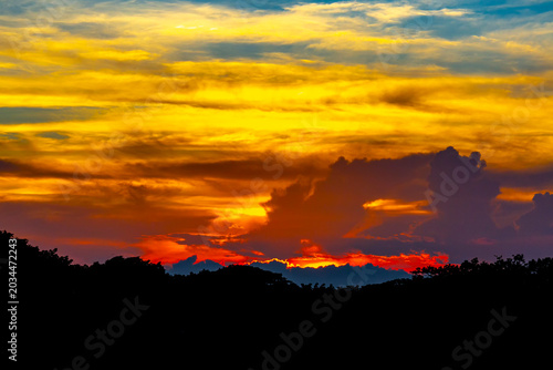 A colorful evening sky scene of blue, orange, yellow, and white at dusk. The silhouette trees and beautiful view of the red sky at dusk.