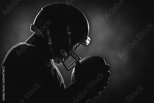 Dramatic silhouette portrait of an American football player holding a ball against a dark background