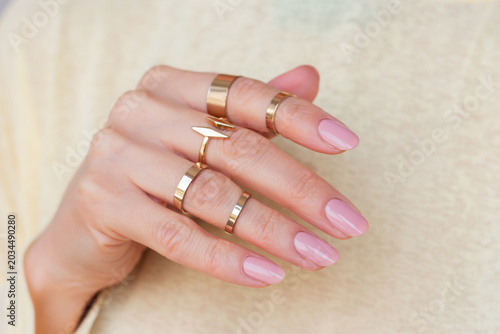 Cuadro en lienzo Woman's hand with a nude manicure, adorned with multiple gold rings on different phalanges of fingers, against a yellow background