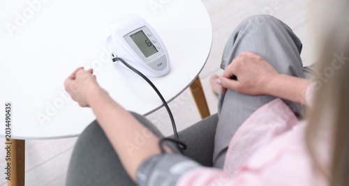 Senior woman measuring blood pressure on sofa at white table, closeup