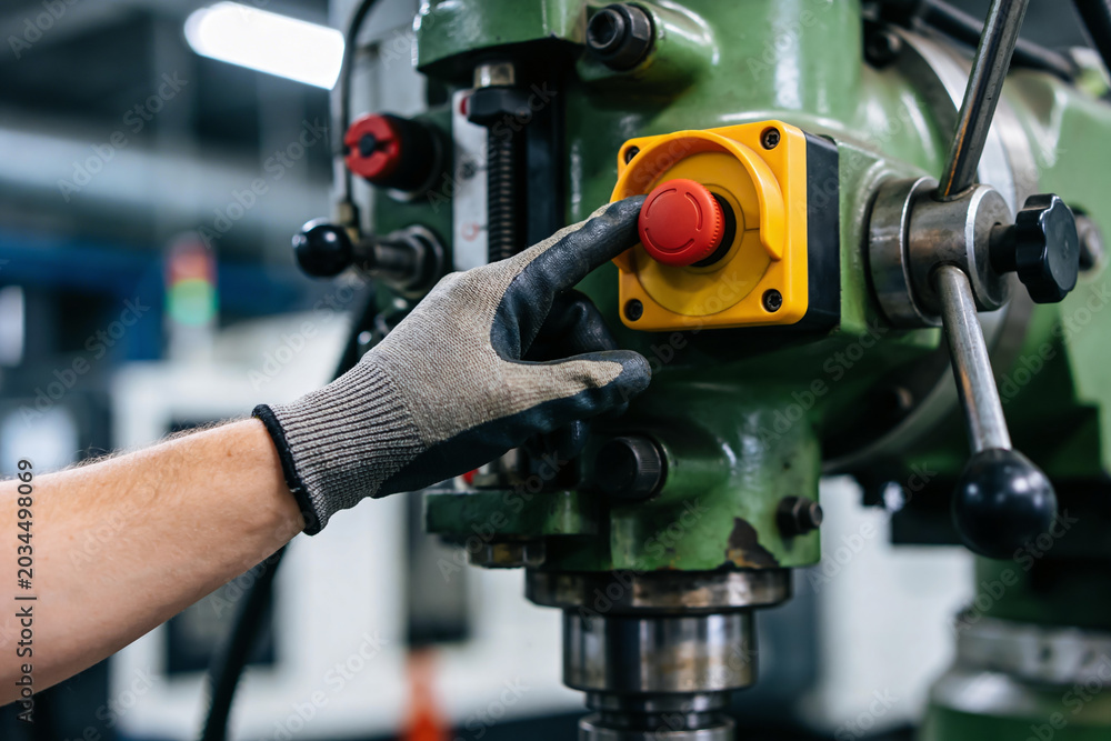 Fototapeta premium Worker presses emergency stop button on industrial machinery in factory setting